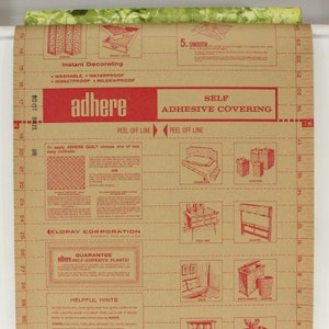 K&ouml;nnte beinhalten: Eine braune Papierrolle mit rotem Text und Illustrationen. Der Text lautet "adhere self adhesive covering" und "instant decorating". Die Illustrationen zeigen verschiedene Haushaltsgegenst&auml;nde, die mit dem Papier bedeckt werden k&ouml;nnen, wie z. B. M&uuml;lleimer, Tischplatten und Dosen.