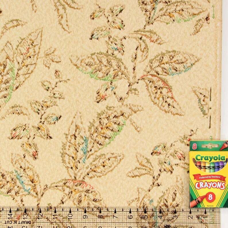 May include: A close-up of a beige wallpaper with a repeating pattern of brown, green, and orange leaves. A ruler and a box of Crayola crayons are visible in the bottom right corner of the image.