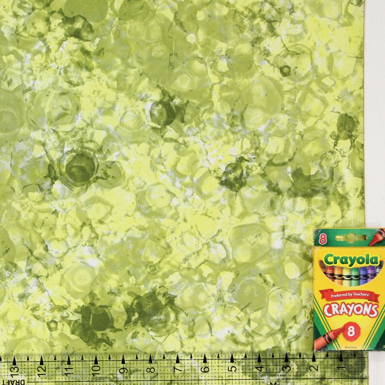 K&ouml;nnte beinhalten: Gr&uuml;ner und gelber Stoff mit einem marmorierten Muster. Eine Schachtel mit 8 Crayola-Stiften befindet sich in der rechten unteren Ecke des Bildes. Die Schachtel ist rot, gelb und blau und tr&auml;gt die Aufschrift "Crayola" und "Crayons".