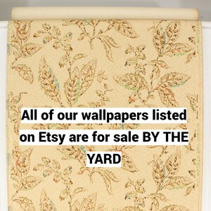 May include: A close-up of a roll of beige wallpaper with a repeating pattern of brown, green, and orange leaves. The text "All of our wallpapers listed on Etsy are for sale BY THE YARD" is printed on the wallpaper.