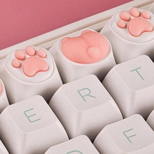 May include: A white keyboard with pink paw print and heart-shaped keycaps. The keys are labeled E, R, T, and F.