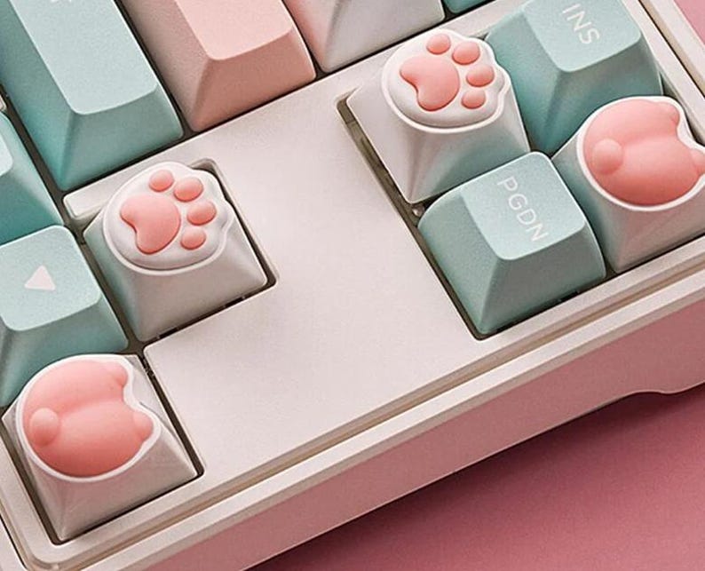 May include: A white keyboard with pastel blue and pink keys. Some of the keys have cute pink paw print keycaps.