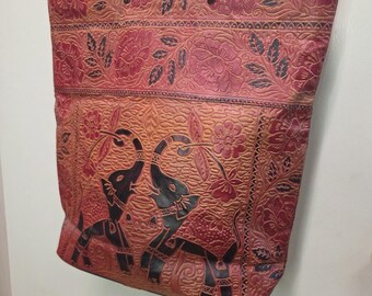 Könnte beinhalten: Eine rechteckige Tragetasche mit einem komplizierten geprägten Design von zwei einander gegenüberstehenden Elefanten, umgeben von Blumenmustern. Die Tasche ist in den Farben Dunkelrot, Orange und Schwarz gehalten und hat zwei dünne Tragegriffe.