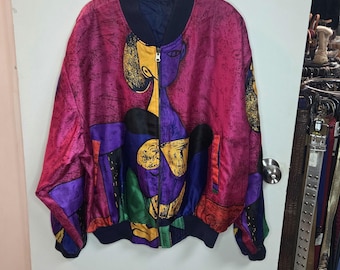 Può includere: Giacca bomber con design artistico astratto. La giacca presenta uno sfondo magenta con un disegno di un volto e forme geometriche in giallo, viola, verde e nero. Ha colletto e polsini neri.