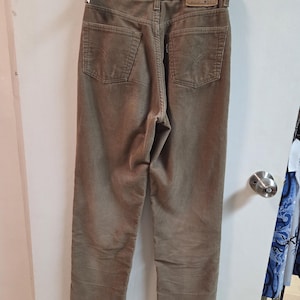 May include: Tan corduroy trousers with a classic five-pocket design. The trousers have a straight leg cut and a Levi Strauss & Co. label on the back. The trousers are hanging on a black hanger.