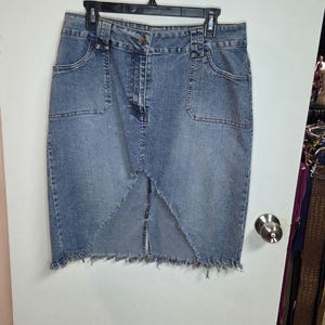 May include: A light blue denim skirt with a frayed hem and front pockets. The skirt has a button and zip closure and is hanging on a black hanger. The skirt is a pencil skirt style.