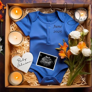 May include: A blue babygrow with the text "June 2025" on the front, a white heart-shaped sign with the text "Baby Johnson", a bouquet of white and orange flowers, and a stack of red blocks with the letters "BABY" on them. The items are arranged in a brown box with straw filling.