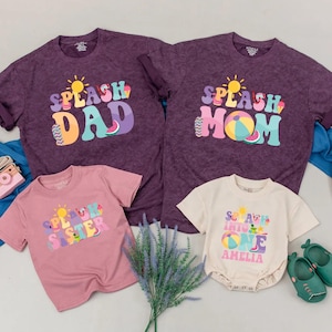 May include: A set of family t-shirts and a baby onesie. The shirts are a vintage purple wash, featuring the phrases "Splash Dad," "Splash Mom," and "Splash Sister." The onesie says "Soak Into One Amelia." There's also a hat and shoes.