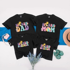 May include: Four black t-shirts with the words "DAD", "MOM", "BROTHER", and "SISTER" in colourful, retro-style lettering. Each shirt has a sun graphic and the word "SPLASH". The shirts are arranged with a camera, hat, and shoes.