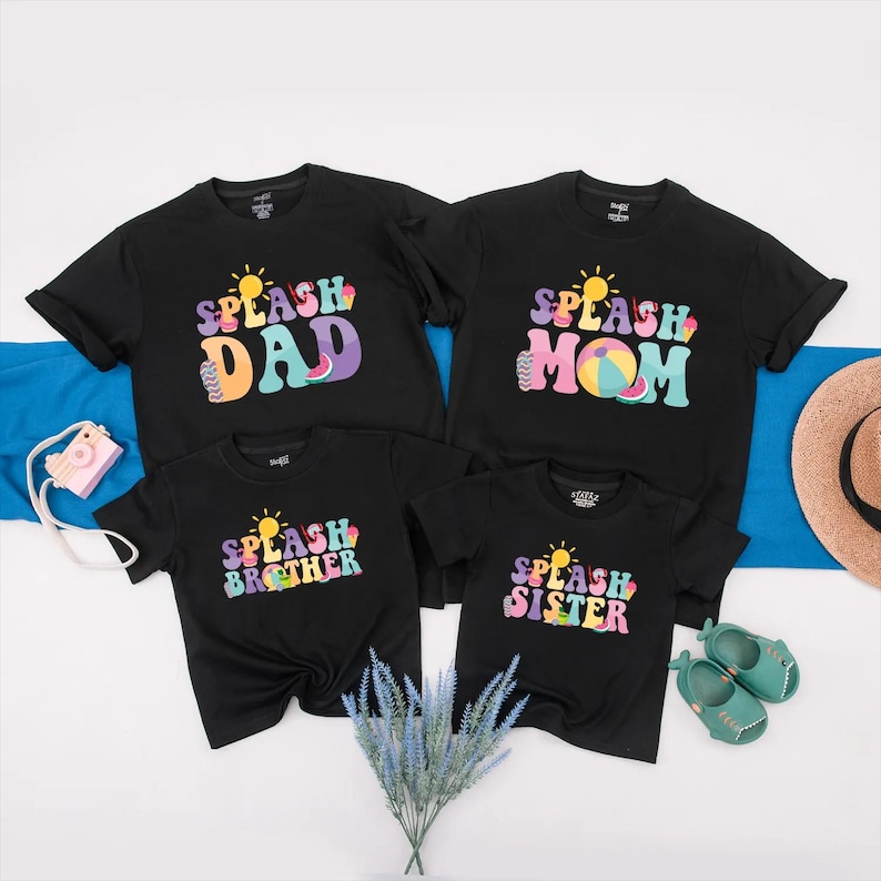 May include: Four black t-shirts with the words "DAD", "MOM", "BROTHER", and "SISTER" in colourful, retro-style lettering. Each shirt has a sun graphic and the word "SPLASH". The shirts are arranged with a camera, hat, and shoes.
