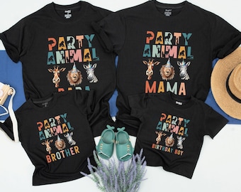 Könnte beinhalten: Vier schwarze T-Shirts mit einem Party-Tier-Motiv. Die Shirts haben unterschiedliche Texte, darunter "Party Animal Dad", "Party Animal Mama", "Party Animal Brother" und "Party Animal Birthday Boy". Jedes Shirt zeigt eine farbenfrohe Grafik einer Giraffe, eines Löwen und eines Zebras, die Partyhüte tragen.