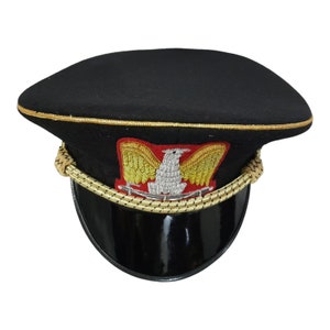 Può includere: Cappello in feltro nero in stile militare con bordatura in passamaneria dorata e un emblema di aquila ricamato in rosso e oro.