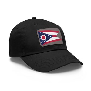 Può includere: Cappellino da baseball nero con una toppa raffigurante la bandiera dell'Ohio. La toppa ha un bordo grigio e mostra il design unico della bandiera, un cerchio circondato da stelle e strisce rosse, bianche e blu.