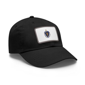May include: Black baseball cap featuring a rectangular patch with the Massachusetts state flag. The patch has a white background with the state seal and a gray border. The cap has a curved brim and a button on top.