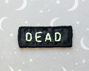 DEAD patch. Handmade embroidered patch. Faux “glow in the dark” embroidery on black ribbon. Hand embroidered fabric word. Dark humor. Sew on