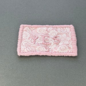 May include: A pink fabric patch with a white floral pattern and the word "YES" embroidered in white thread.