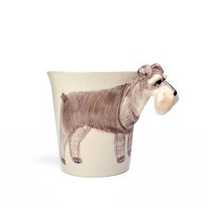 May include: A ceramic coffee mug with a brown and white miniature schnauzer dog handle. The dog's head is sculpted in 3D and the body is painted on the mug.