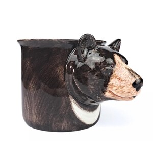 Könnte beinhalten: Eine braune Keramiktasse in Form eines Bärenkopfes. Die Tasse hat einen weißen Streifen um den Hals und eine schwarze Nase.
