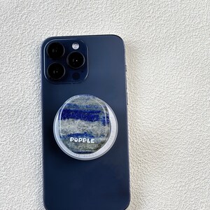 May include: A dark blue phone case with a round, white phone grip. The grip has a blue and white marbled design and the word "POPPLE" printed on it.