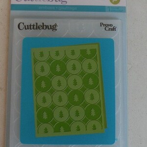 May include: A blue and white plastic package containing a Cufflebug embossing folder with a pattern of green trees in circles. The package includes the text "Winter Trees" and "Arbres de l'Hiver".