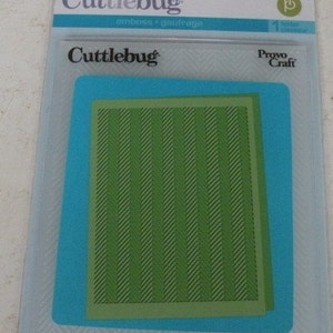 May include: A green plastic embossing folder with a herringbone pattern. The folder is packaged in a clear plastic sleeve with the brand name "Cuttlebug" and the text "emboss - gaufrage".