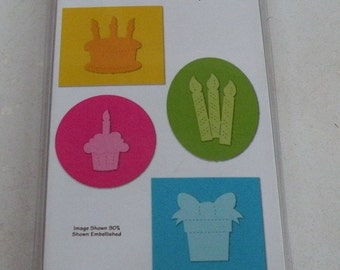 May include: A package of four Sizzlits dies for crafting. The dies are designed to cut out birthday-themed shapes, including a cake, candles, a cupcake, and a gift box. The package is red, white, and blue with the Sizzix logo and the text "Sizzlits" in white. The package also includes the text "Birthday Knockout, Anniversaire de Folie, Cumpleaño de Locura" and the designer's name "Emily Humble".