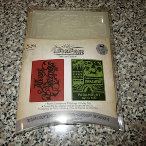 May include: A clear plastic embossing folder set with a red and green Christmas theme. The set includes designs with the text "Merry Christmas" and "Ornaments". The package also includes the text "Texture Fades".