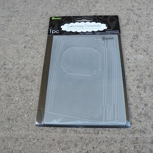 May include: A clear plastic embossing folder with a decorative frame design. The folder is packaged in a clear plastic sleeve with a black and white label that reads "Embossing Essentials" and "Darice".