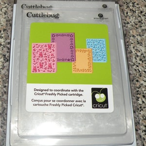 May include: A set of four Cuttlebug embossing folders designed to coordinate with the Cricut Freshly Picked cartridge. The folders are in a clear plastic package with a green background and the Cricut logo. The folders are pink, orange, blue, and purple.