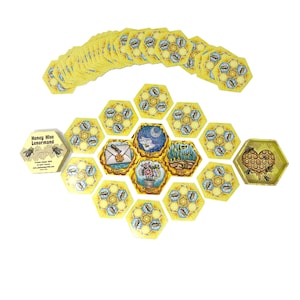 May include: Honey Hive Lenormand deck of cards with a honeycomb design. The cards are laid out in a circle with a hexagonal shape. The cards are yellow and blue with illustrations of bees, flowers, and other symbols.