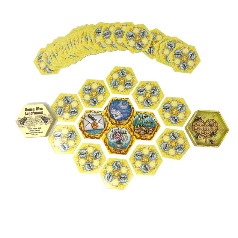 May include: Honey Hive Lenormand deck of cards with a honeycomb design. The cards are laid out in a circle with a hexagonal shape. The cards are yellow and blue with illustrations of bees, flowers, and other symbols.
