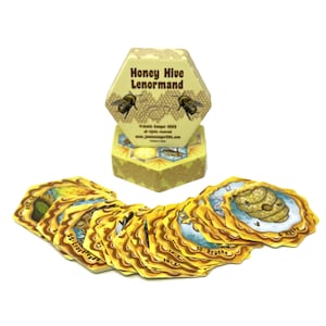 May include: A yellow and brown hexagonal box with the text "Honey Hive Lenormand" on the front. The box is open and contains a deck of 36 cards with yellow and brown honeycomb designs. The cards are arranged in a fan shape.