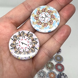 May include: Two circular pin-back buttons featuring illustrations. One button displays a ring of goldfish with the number 34 in the center. The other button shows a ring of horses with riders and the number 1 in the center. Additional buttons are visible.