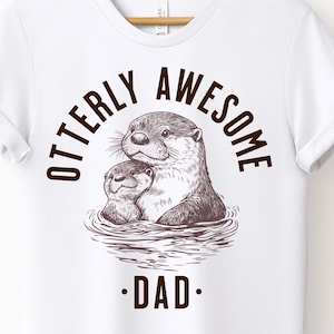 May include: White t-shirt with a brown graphic of two otters hugging. The text "Otterly Awesome .DAD." is printed on the shirt.