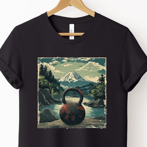 May include: Black t-shirt featuring a vintage-style illustration of a kettlebell in front of a mountain landscape. The kettlebell is red and rusty, and the mountain is green and blue.