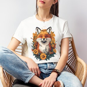 una donna seduta con una maglia bianca con l'immagine di una volpe sorridente circondata da fiori in stile cottagecore