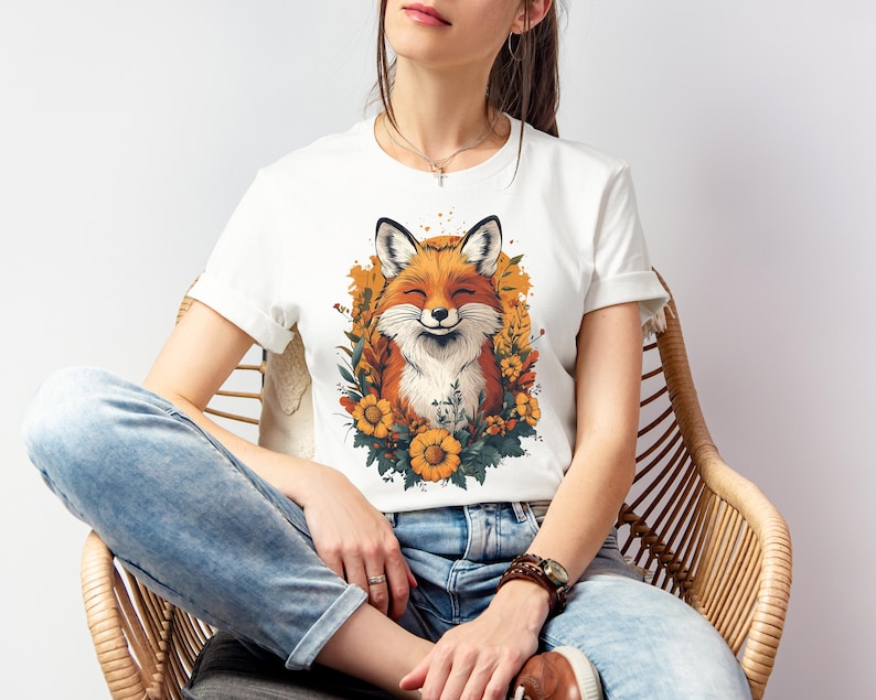 una donna seduta con una maglia bianca con l'immagine di una volpe sorridente circondata da fiori in stile cottagecore