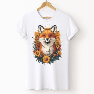 una maglia bianca con l'immagine di una volpe sorridente circondata da fiori in stile cottagecore
