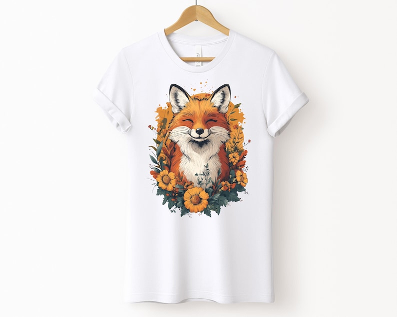 una maglia bianca con l'immagine di una volpe sorridente circondata da fiori in stile cottagecore