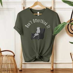 una tshirt color verde militare con una lontra su una poltrona e sopra di lei la scritta "Don't otterthink it"