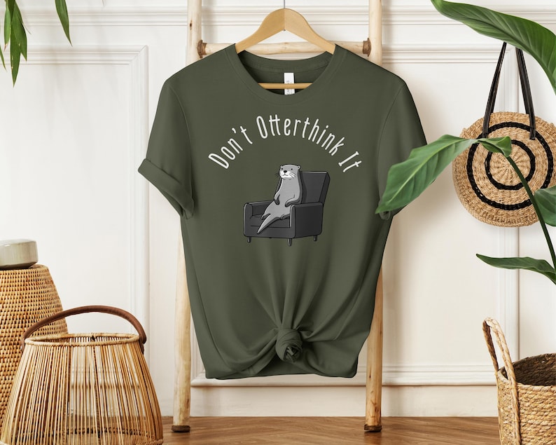 una tshirt color verde militare con una lontra su una poltrona e sopra di lei la scritta "Don't otterthink it"