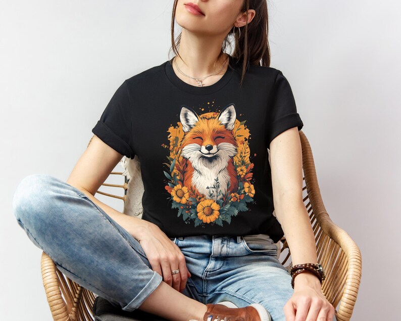 una donna seduta con una maglia nera con l'immagine di una volpe sorridente circondata da fiori in stile cottagecore