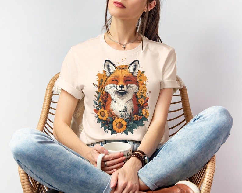 una donna seduta con una maglia color crema con l'immagine di una volpe sorridente circondata da fiori in stile cottagecore