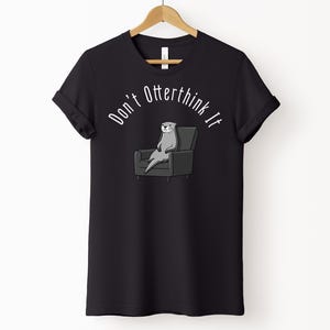 una tshirt nera con una lontra su una poltrona e sopra di lei la scritta "Don't otterthink it"