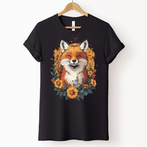 una maglia nera con l'immagine di una volpe sorridente circondata da fiori in stile cottagecore