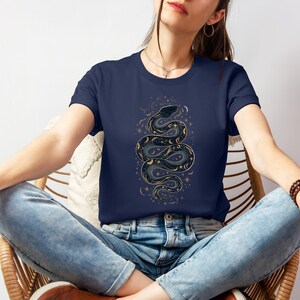 una donna con una t-shirt color marina militare con la silhouette di un serpente formata da stelle, lune e soli