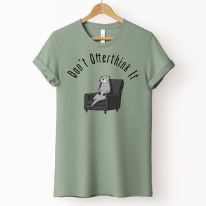 una tshirt color sage con una lontra su una poltrona e sopra di lei la scritta "Don't otterthink it"