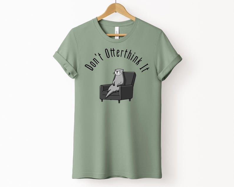 una tshirt color sage con una lontra su una poltrona e sopra di lei la scritta "Don't otterthink it"