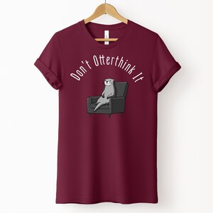 una tshirt color marroon con una lontra su una poltrona e sopra di lei la scritta "Don't otterthink it"