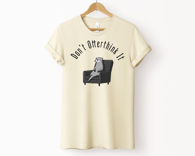 una tshirt color naturale con una lontra su una poltrona e sopra di lei la scritta "Don't otterthink it"